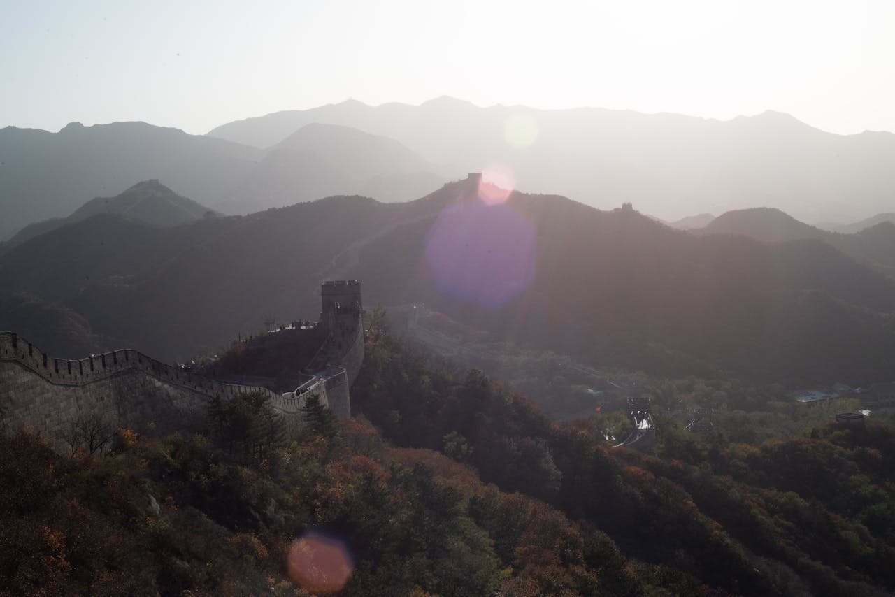 Stunning view of the Great Wall of China with sun glare, mountains, and scenic wilderness.