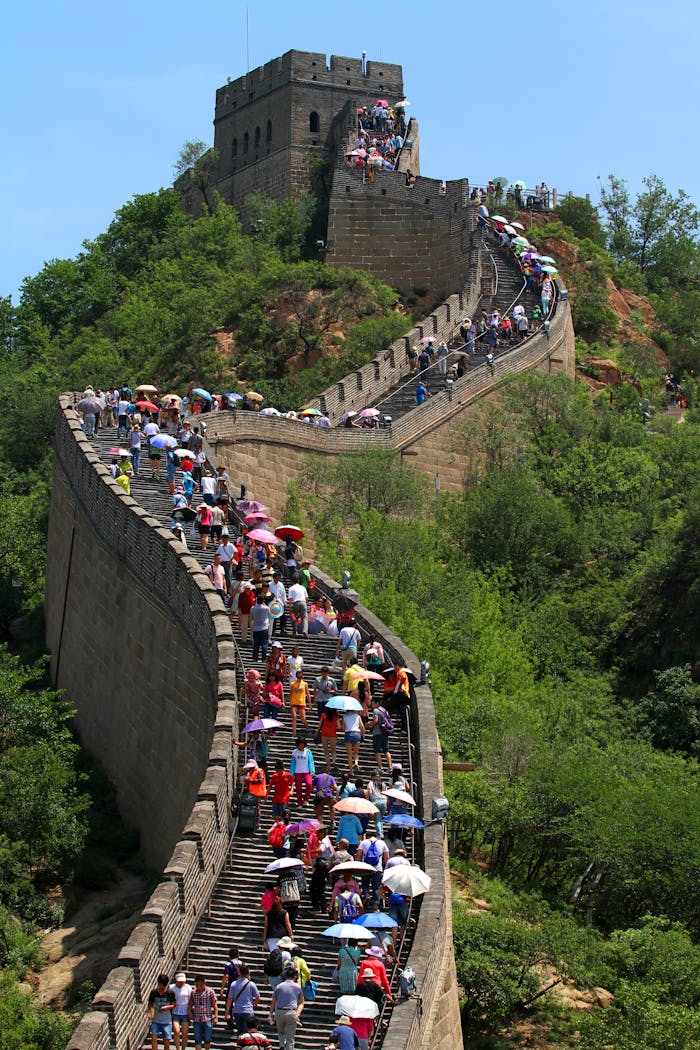 Tourists walk along the Great Wall of China amid lush greenery on a sunny day.